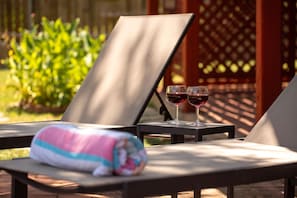 A sunlit outdoor seating area with lounge chairs, a towel, and two glasses of red wine. - 5BR San Antonio Home - Large Private Pool, Covered Patio, BBQ & Outdoor Games (San Antonio)