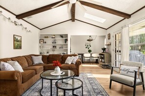 Ein geräumiges Wohnzimmer mit hoher Decke, einer braunen Sofagarnitur, einem Glastisch und einem Essbereich mit einer Chandelüster.