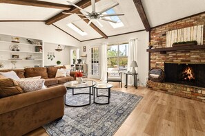 Ein geräumiges Wohnzimmer mit Kamin, Deckenventilator und großem Fenster.