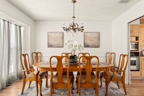 Une salle à manger avec une table ronde en bois entourée de six chaises, un lustre et deux tableaux abstraits accrochés au mur.