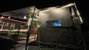 En bygning med facade af bølget metal, en trappe op til et overdækket område, og et vindue med udsigt til indretningen indeni.