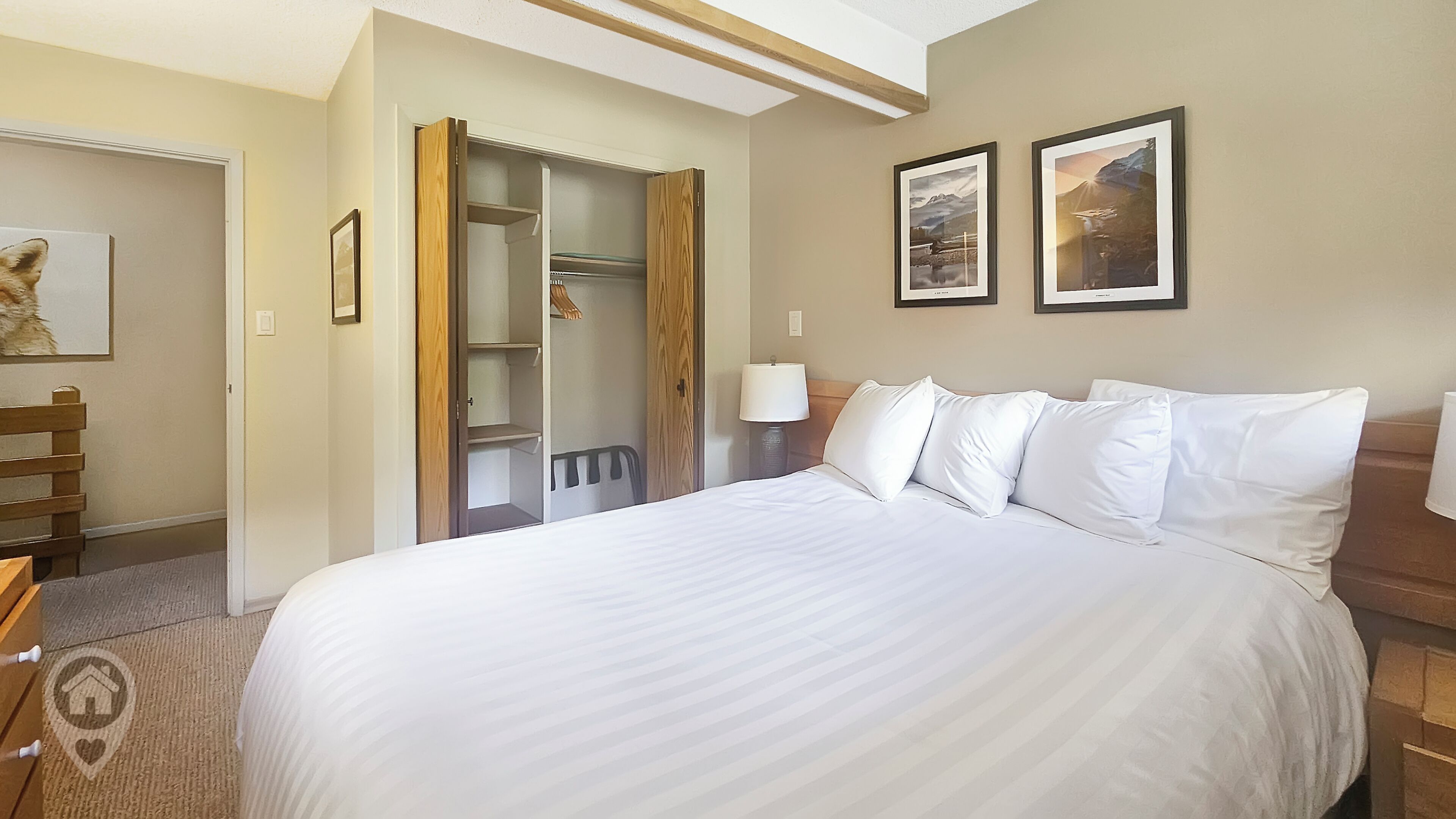 A hotel room with a large bed, a wooden bench, a wardrobe, and two framed pictures on the wall.