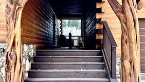 Eine Holztreppe mit rustikalem Design, gesäumt von dicken Baumstämmen, die zu einem überdachten Eingang führt.