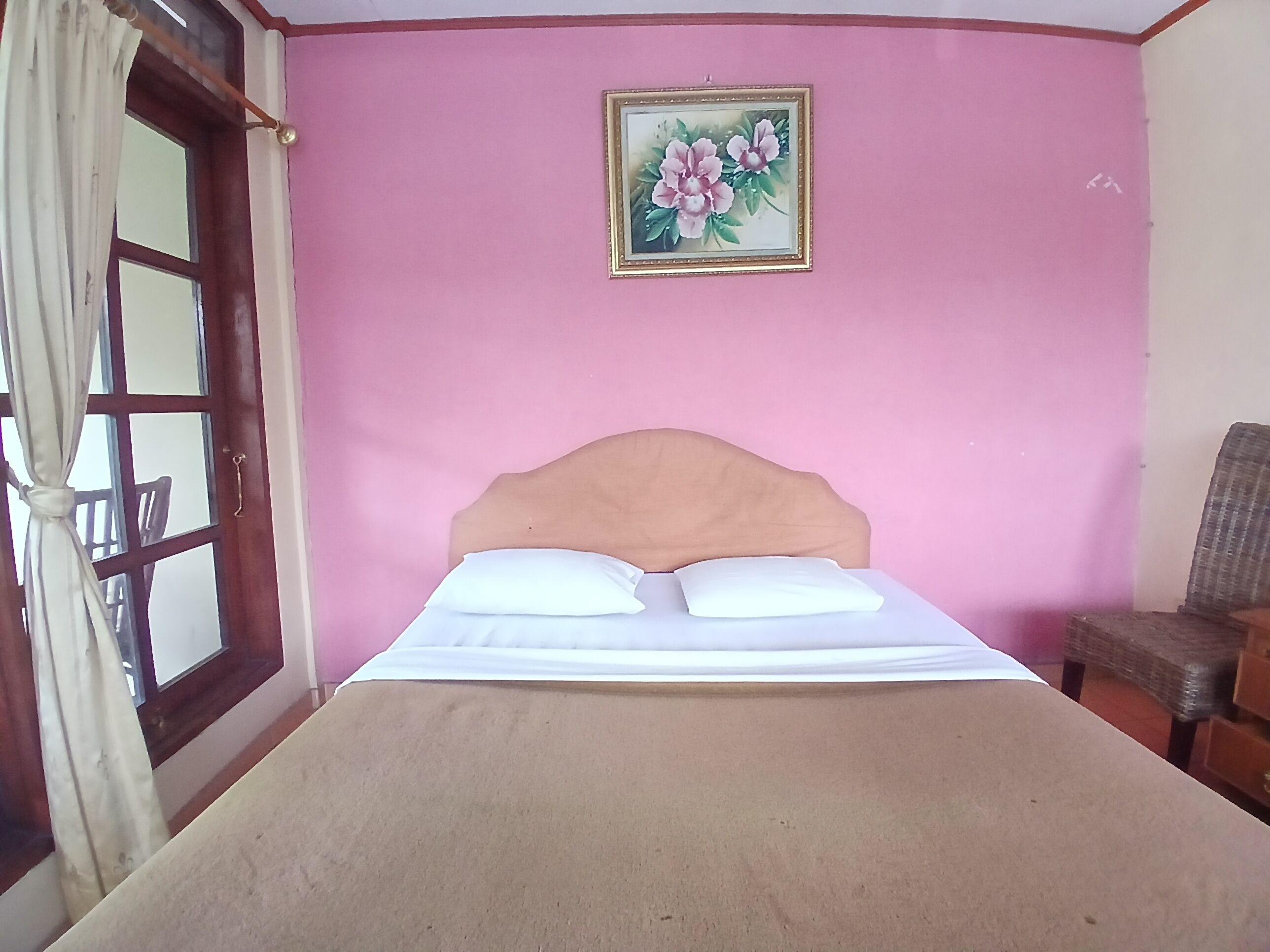 A room with a bed, a window with curtains, a chair, and a framed picture on the wall.