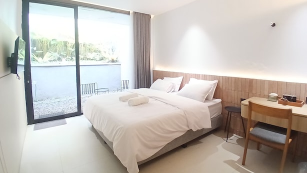 A modern hotel room with a large bed, a desk, and a view of a pool and greenery. - Cibulan Indah Hotel (Cisarua)