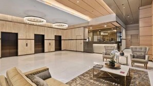 A spacious lobby with a modern design, featuring a central seating area with sofas and armchairs, a chandelier, and a reception desk. - Million Dollar Views Luxury Apartment with 3pm Late Checkout (South Brisbane)