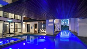 Un espace piscine intérieur moderne avec vue sur la ville, un comptoir d’accueil et des chaises longues.