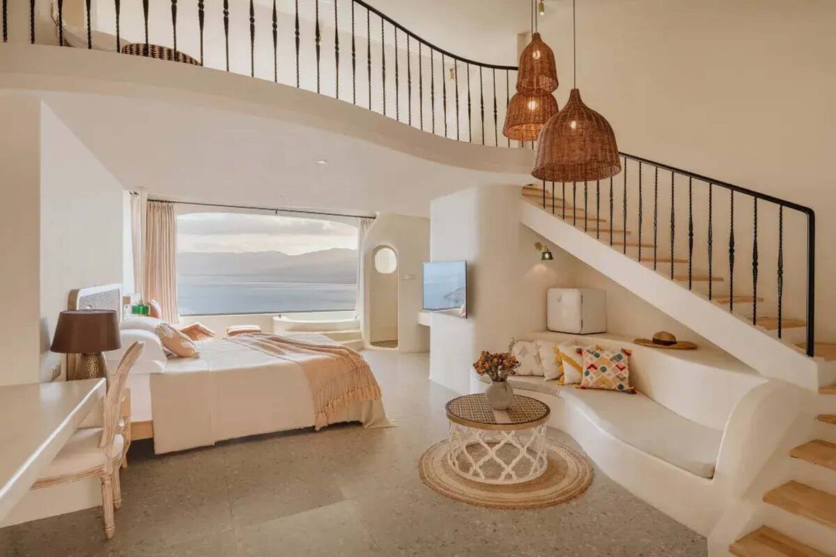 Ein geräumiges Schlafzimmer mit einem großen Bett, einer Sitzecke mit einer Couch, einem runden Couchtisch und einer Treppe mit Geländer.