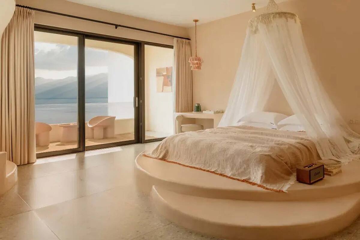 Ein Schlafzimmer mit einem bogenförmigen Bett, einem Baldachin, einem Schreibtisch und Meerblick.