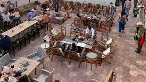 Een buitenterras met tafels en stoelen, een podium voor optredens, en uitzicht op de ondergaande zon.