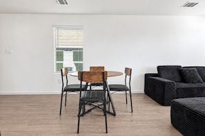 A modern living room with a round table and four chairs, a black sofa, and a window with blinds. - 3BR Near Gruene Historic District, Comal, and Guadalupe Rivers & Schlitterbahn (New Braunfels)