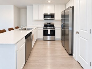 A modern kitchen with white cabinets, stainless steel appliances, and a wooden floor. - 3BR Near Gruene Historic District, Comal, and Guadalupe Rivers & Schlitterbahn (New Braunfels)