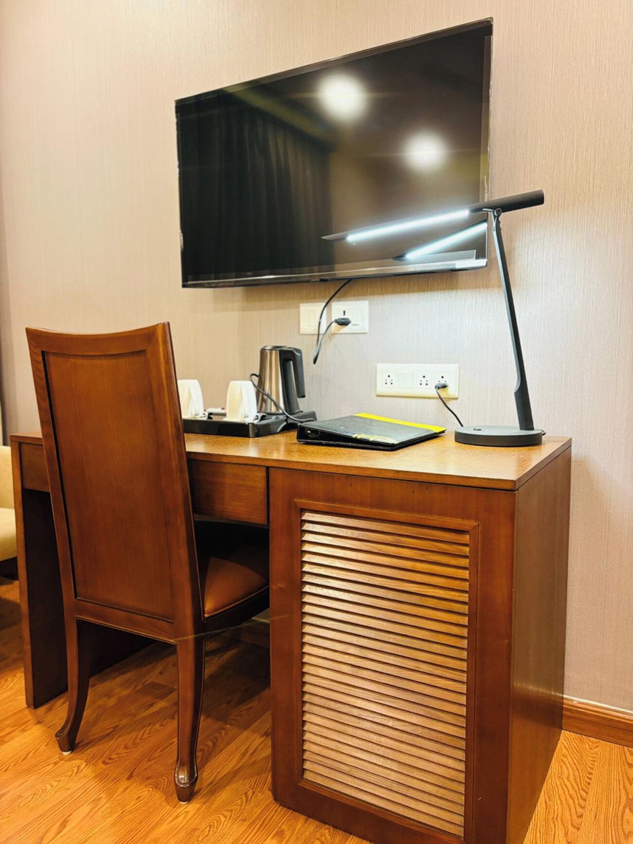 A wooden desk with a flat-screen TV, a lamp, and a coffee maker.