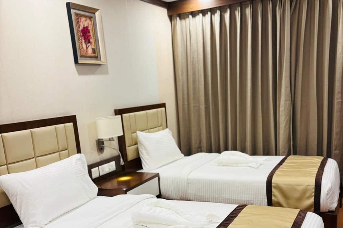 Une chambre d’hôtel avec deux lits, un ventilateur de plafond, un tableau encadré au mur et une fenêtre avec des rideaux.