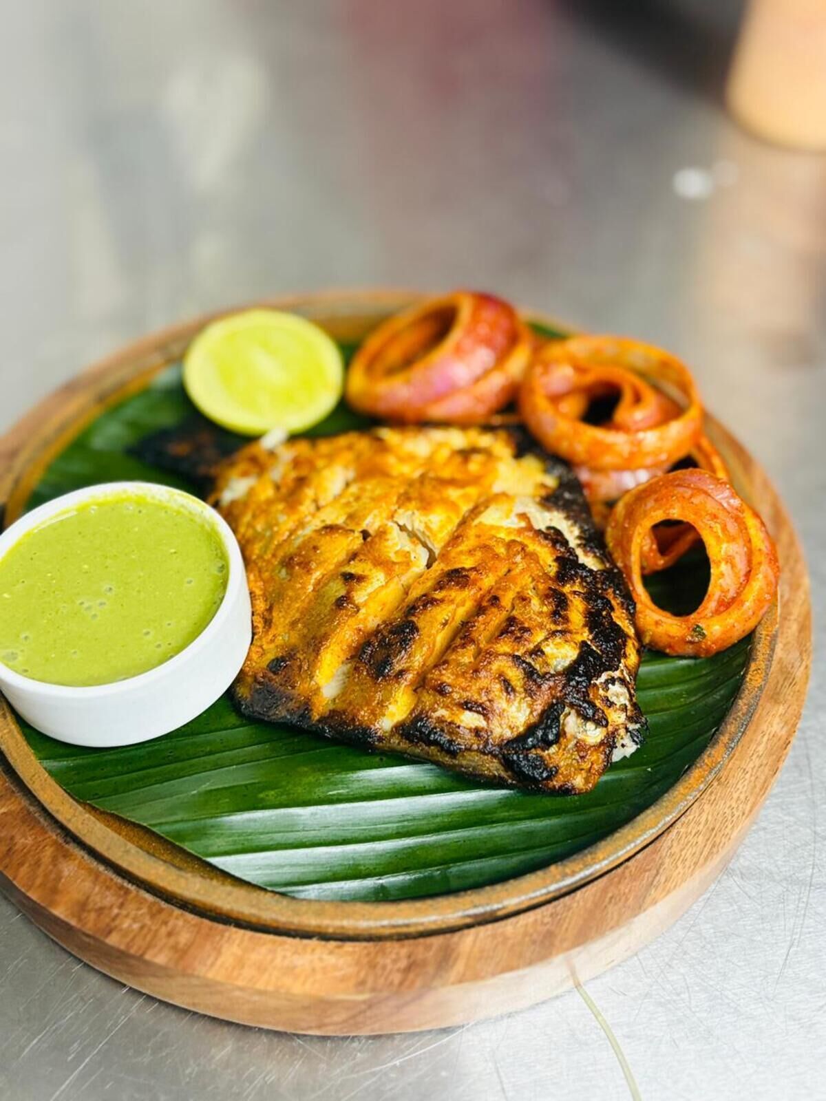 A plate of grilled fish with onion rings and a green sauce on a wooden board.