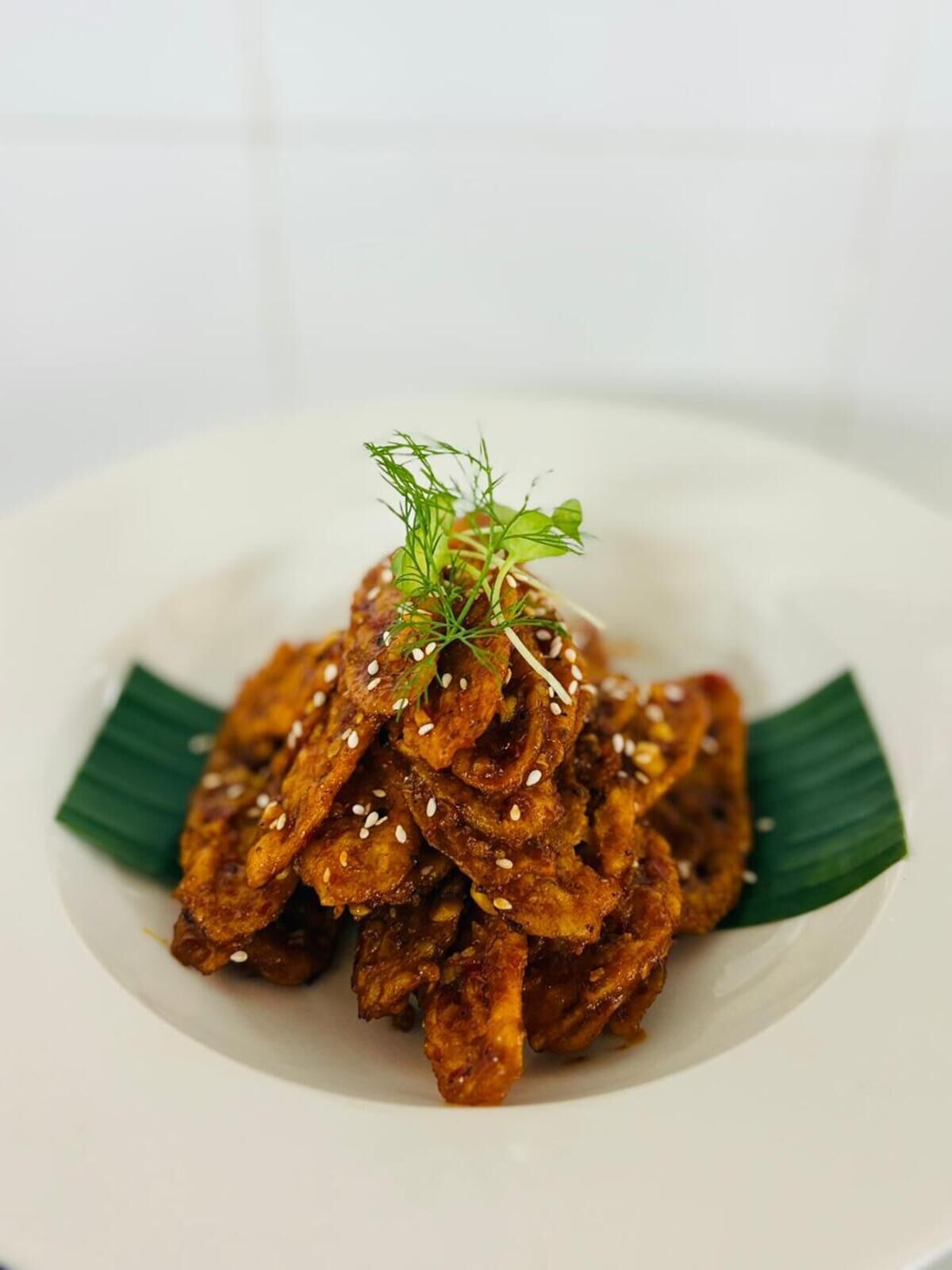 A plate of crispy fried chicken garnished with sesame seeds and a sprig of green herb.