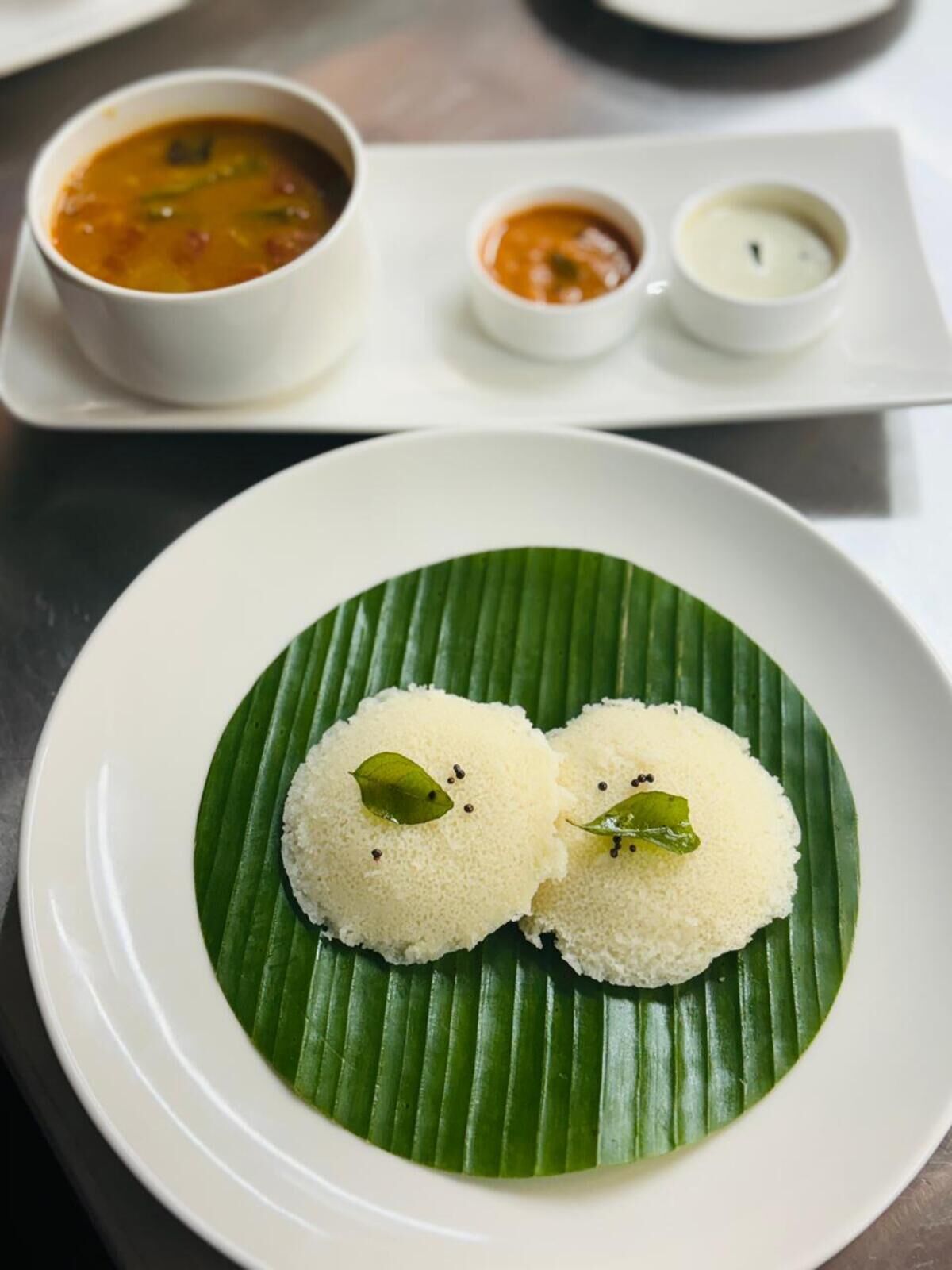 A plate of idlis with chutney and sambar.
