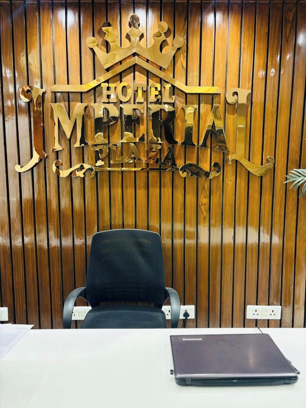 A reception desk with a laptop, a chair, and a wooden panel wall with a crown and "HOTEL MEXICO" sign.