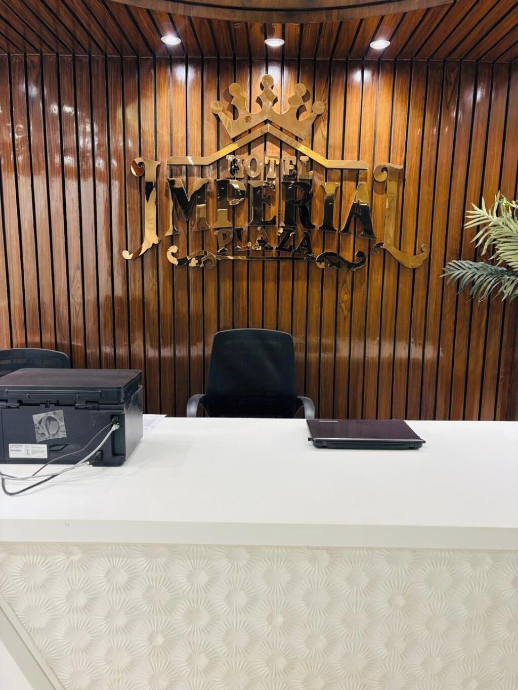 A reception desk with a wooden panel wall, a crown-shaped sign reading "IMPERIA," and a laptop on the desk.