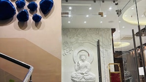 Een modern interieur met een glazen wand waarop een Boeddhabeeld staat, een trap met glazen balustrades en blauwe decoratieve elementen aan de wand.