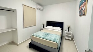 Ein Schlafzimmer mit einem Bett, Nachttischen, einer Wandklimaanlage und einem Bild an der Wand.