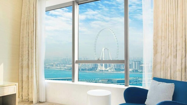 Ein Zimmer mit großem Fenster und Blick auf eine Stadtlandschaft, darunter ein großes Riesenrad.