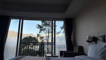 Habitació d'hotel amb un llit gran, una tauleta de nit, una cadira i vista a les muntanyes a través de grans finestres.