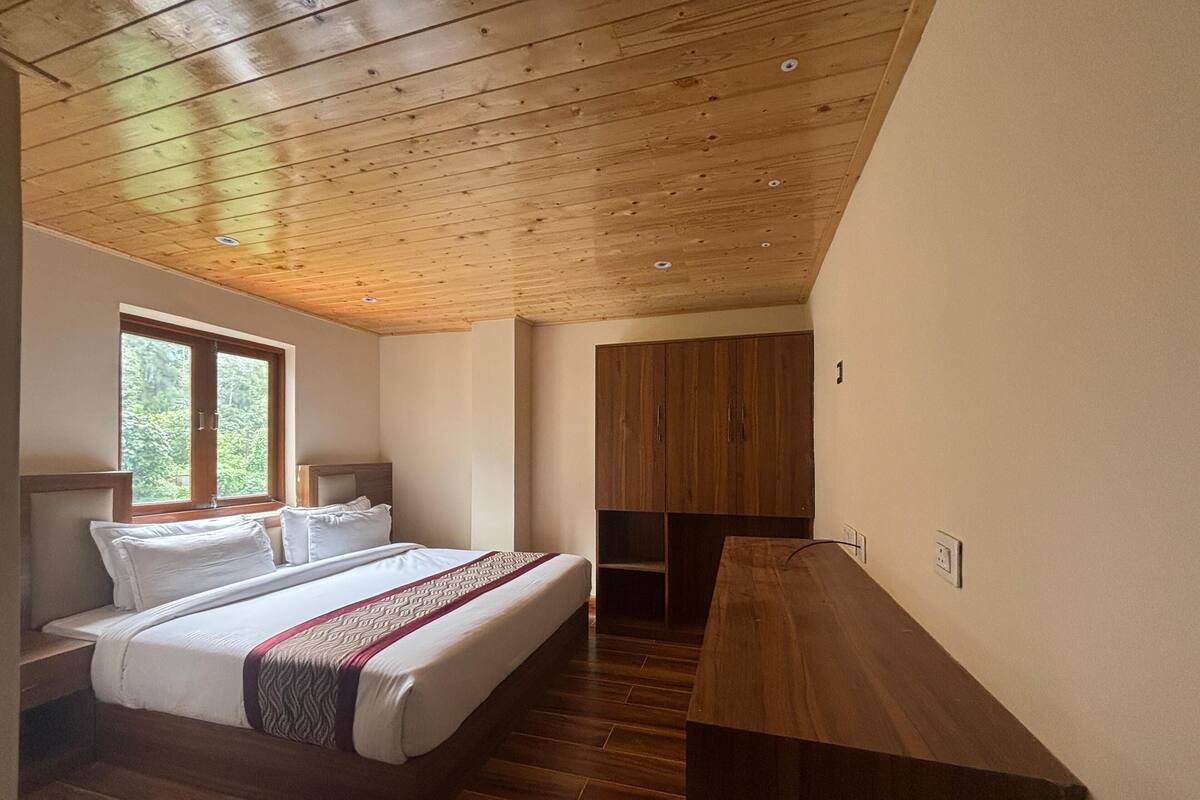 Ein Schlafzimmer mit Holzbalkendecke, einem Bett mit weißer Bettwäsche, einem Fenster mit Blick ins Grüne und einem Holzschrank.