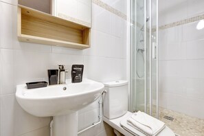 A modern bathroom with a white sink, a glass shower enclosure, and a wooden shelf above the sink. - TBS 98 - Superb terrace apartment in Paris 15 (Paris)