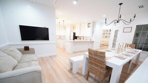 Moderni olohuone, jossa on sohva, ruokapöytä, joka on katettu valmiiksi ateriaa varten, ja taustalla keittiö.