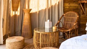 A room with a wicker chair, a round table, and two wicker ottomans. - Whispering Woods (Bhiwandi)