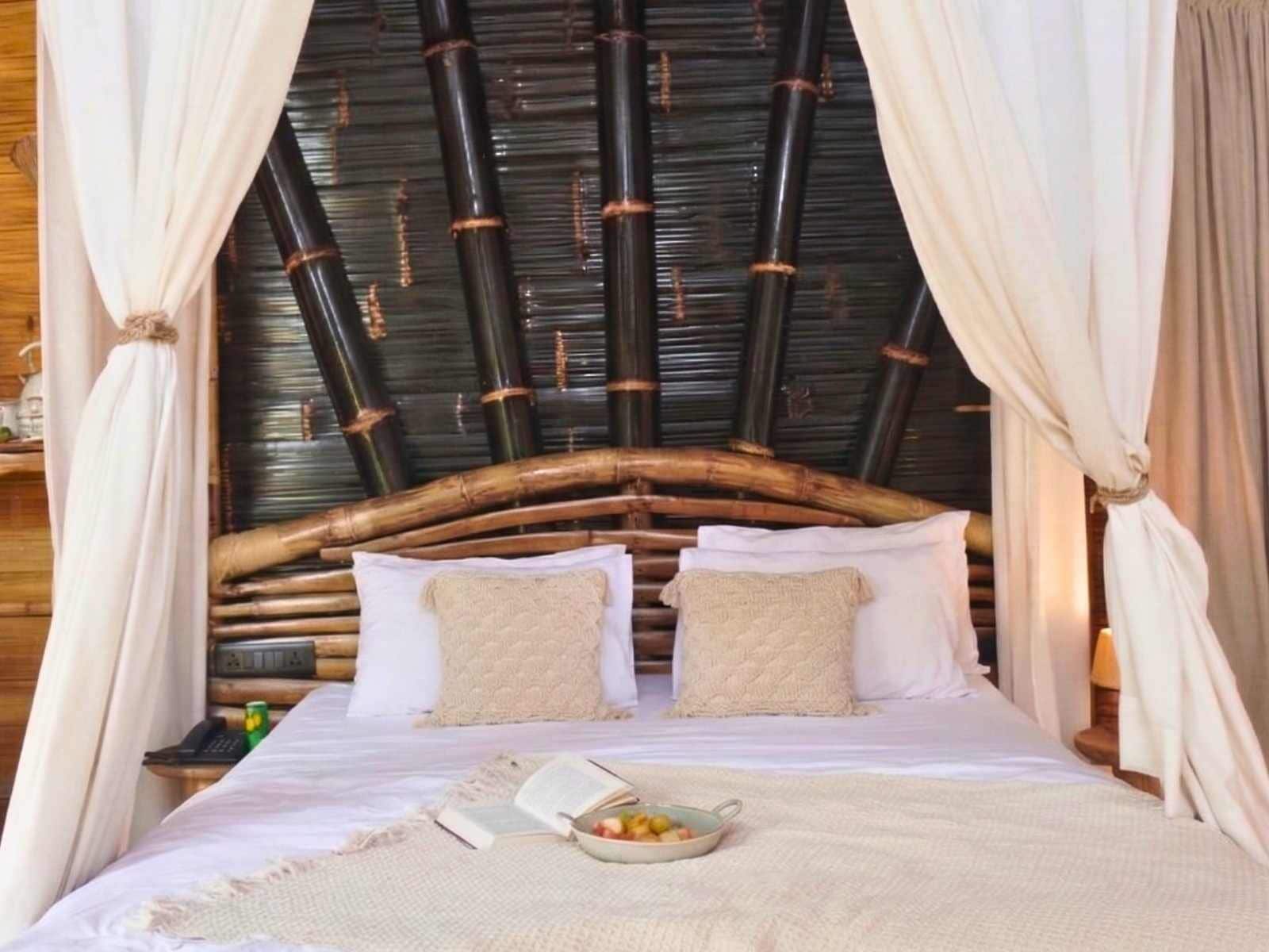 Uma cama com cabeceira de fibra natural, roupa de cama branca e uma tigela de fruta na mesa de cabeceira.