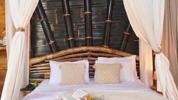 Uma cama com cabeceira de fibra natural, roupa de cama branca e uma tigela de fruta na mesa de cabeceira.