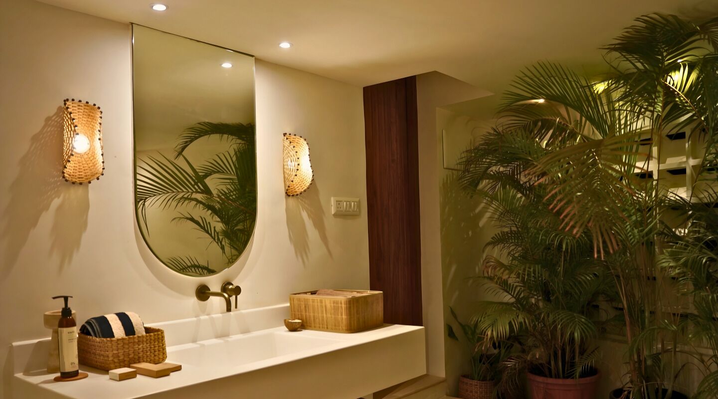 Een badkamer met een grote spiegel, twee wandlampen, een houten wastafelmeubel en een potpalm.