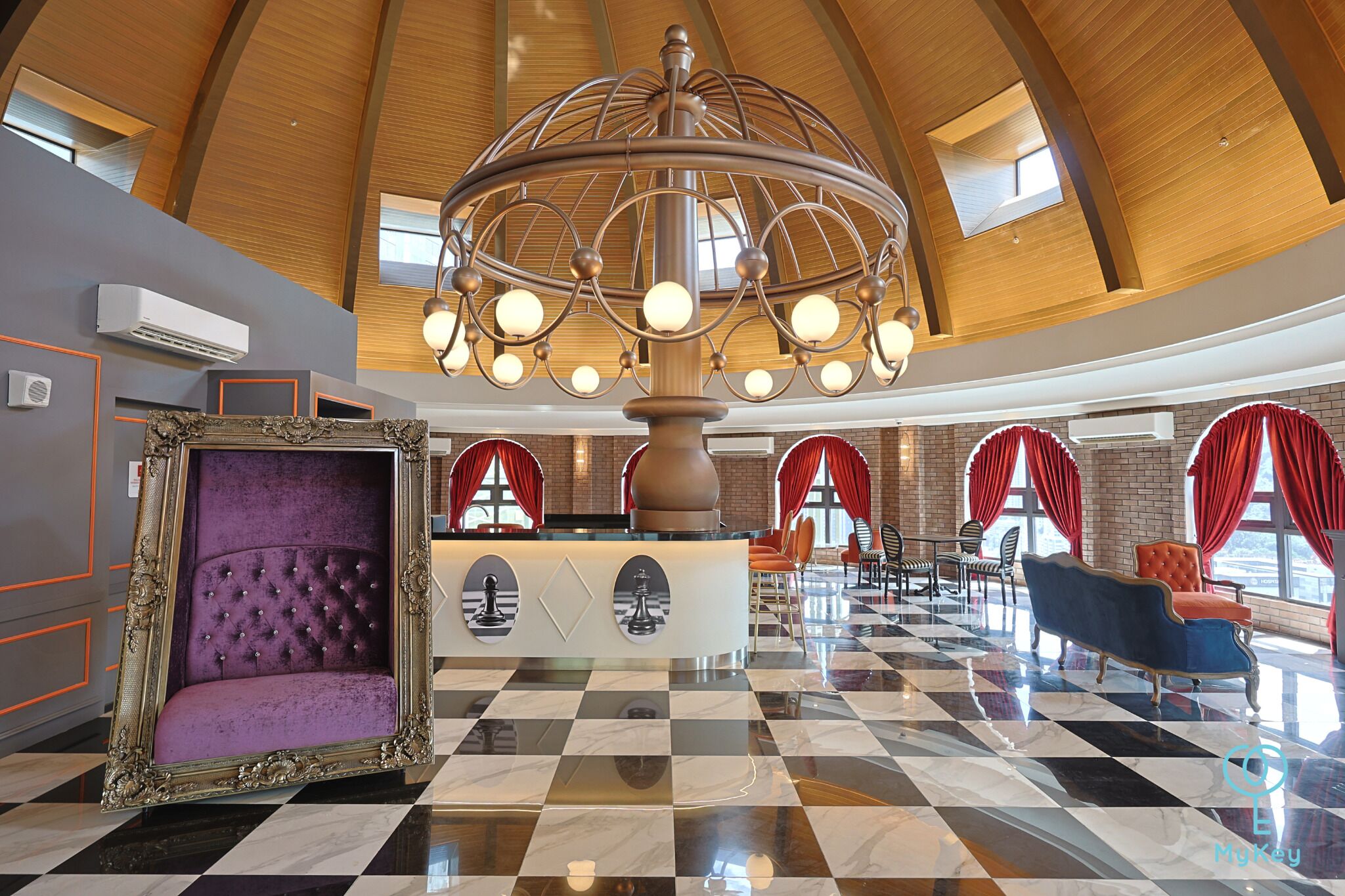 A lobby with a checkered floor, a large chandelier, red curtains, and a purple upholstered chair.