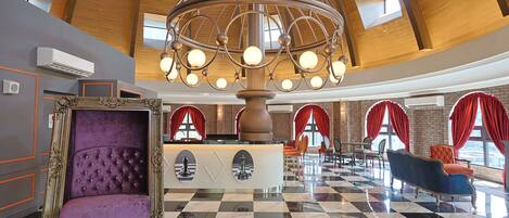 A lobby with a checkered floor, a large chandelier, red curtains, and a purple upholstered chair.
