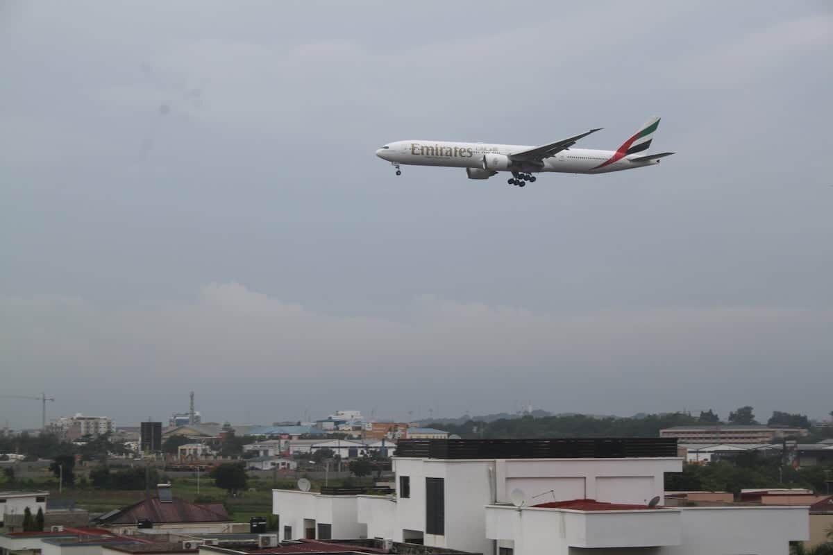 Ein Emirates-Flugzeug fliegt über einer Stadtlandschaft mit modernen Gebäuden.