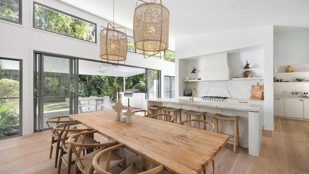 Eine moderne Küche mit Holztisch und Stühlen, weißen Schränken und großen Fenstern mit Blick auf einen Garten.