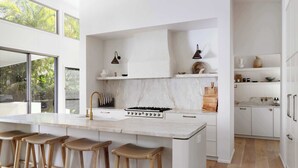 Eine moderne Küche mit einer großen Kochinsel, Barhocker, einem Gasherd und Blick auf Grünflächen.