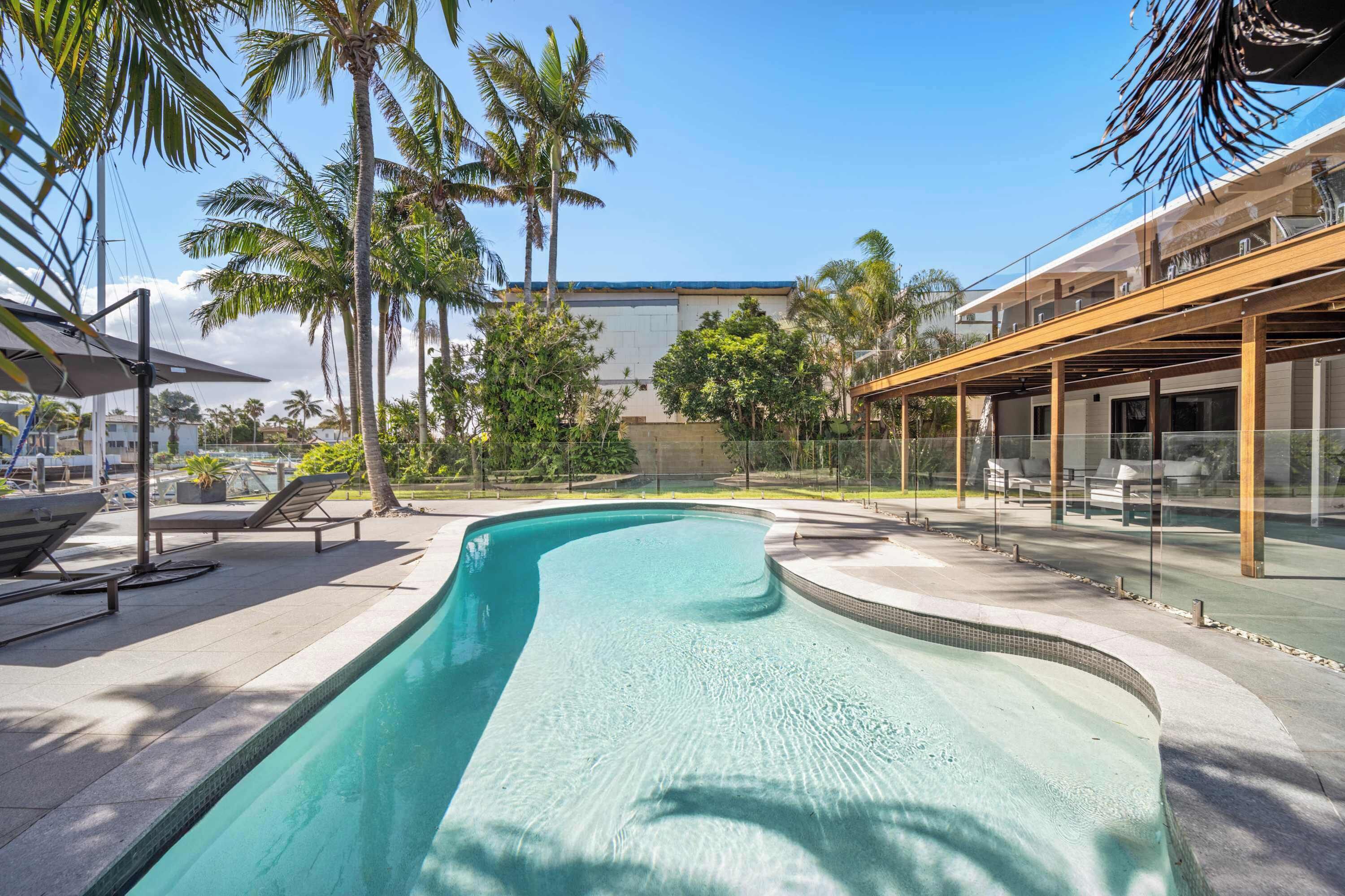 A swimming pool with lounge chairs, palm trees, and a covered outdoor seating area.