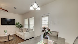 A modern living room with a dining table, a sofa, and a TV mounted on the wall. - Suburban San Antonio Stay Near Parks & Hospitals (San Antonio)