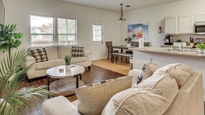 A spacious living room with a sofa, a coffee table, and a dining area with a bench. There is a kitchen area with cabinets and a microwave. - Suburban San Antonio Stay Near Parks & Hospitals (San Antonio)