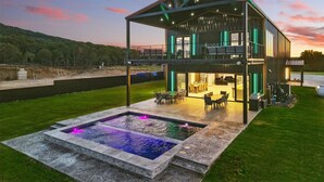 A modern two-story house with a pool and outdoor seating area. - Lakefront resort home. Sleeps 26+! Boat dock, kayaks, pool, hot tub & more! (Graham)