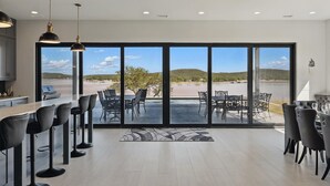 A modern kitchen with a bar area, large sliding glass doors leading to an outdoor patio with seating. - Lakefront resort home. Sleeps 26+! Boat dock, kayaks, pool, hot tub & more! (Graham)