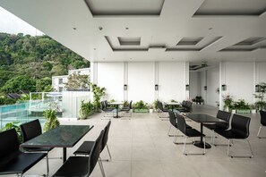 A modern outdoor dining area with glass tables and black chairs, surrounded by potted plants and overlooking a pool and lush greenery. - Seavale Patong Phuket (Patong)