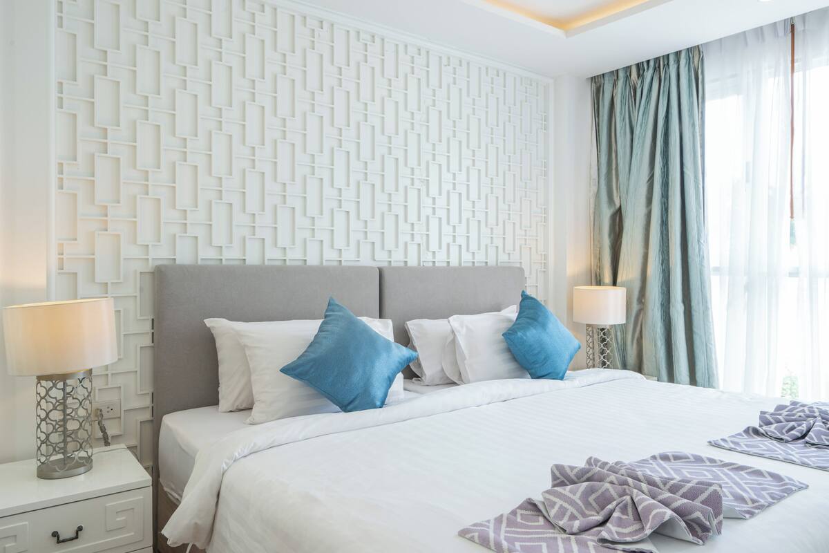 A neatly made bed with white and blue pillows, a grey headboard, and a patterned wall.