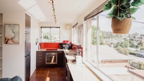 A modern kitchen with a large window, a hanging plant, and a view of the city. - Valley View 6 | Lenah Valley (Hobart City)