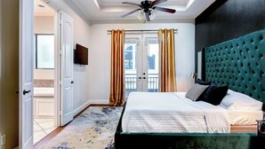 Un dormitorio con cama, ventilador de techo, televisión y vistas al exterior a través de una ventana con cortinas.