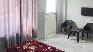 Ein Hotelzimmer mit Bett, Fernseher, Schreibtisch, zwei Stühlen, Klimaanlage und einer Tür.