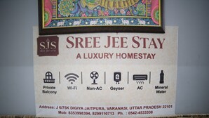 Schild für Sree JEE Stay, ein luxuriöses Gästehaus, mit aufgelisteten Annehmlichkeiten wie privatem Balkon, WLAN, ohne Klimaanlage, Boiler, Klimaanlage und Mineralwasser.